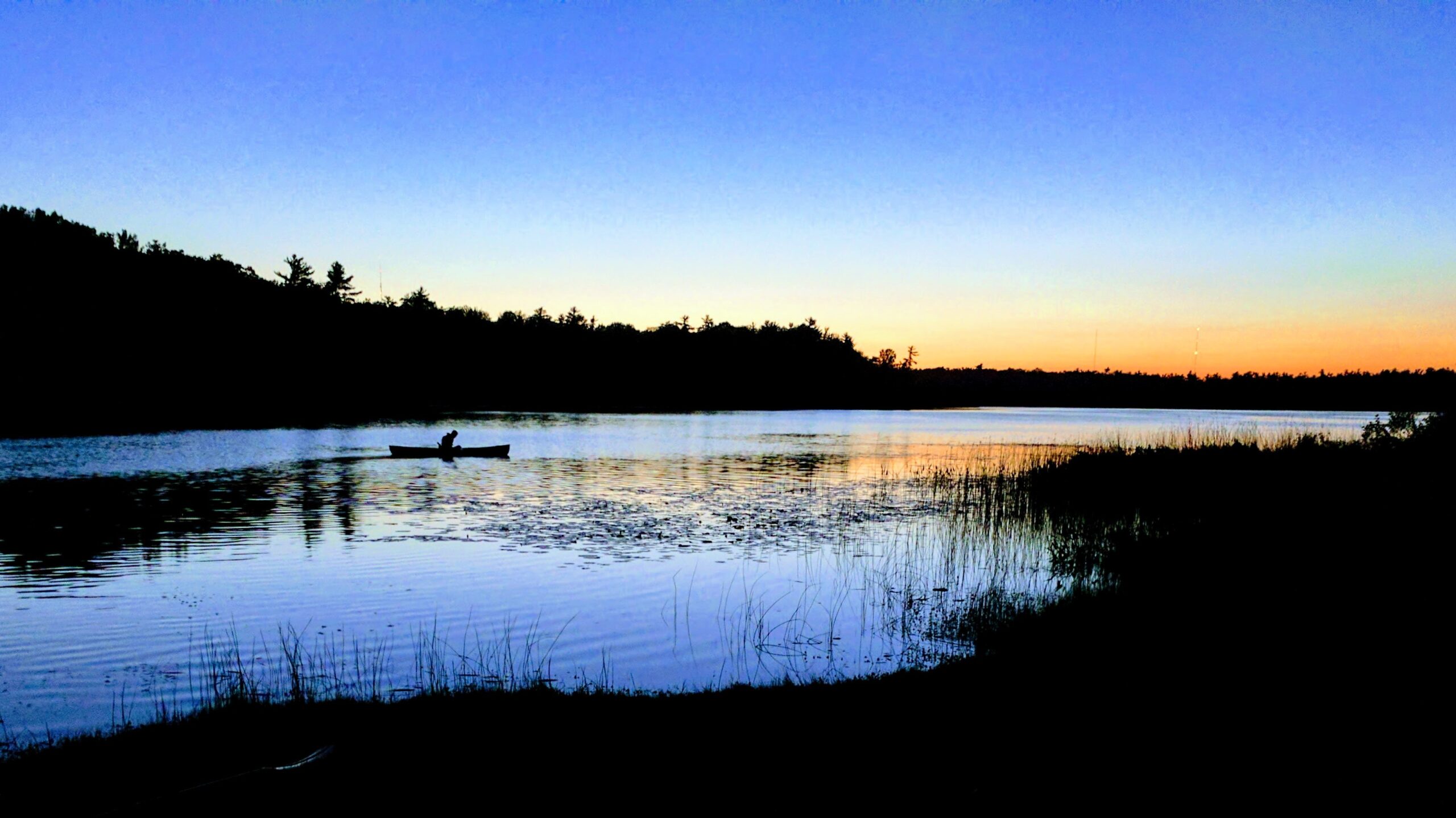 A lone conue on a blue lake at sunset.